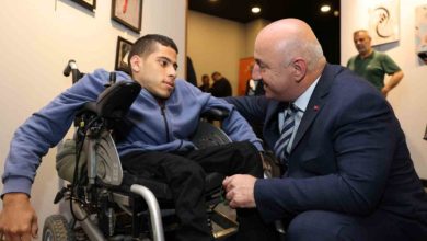 Başkan Muzaffer Bıyık, akülü tekerlekli sandalye kullanıcısı engelli erkek gençle yüz yüze seviyesinde sohbet ediyor.