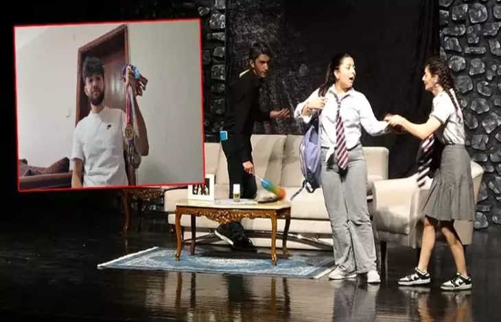 Bir sahne üzerinde üç genç oyuncu, okul kıyafetleriyle tiyatro performansı sergiliyor. Arkada kanepe ve masa bulunan bir salon dekoru yer alıyor. Görselin sol köşesinde ise bir erkek, elinde madalyalarla kameraya poz verirken görülüyor. Sahne enerjik ve duygusal bir atmosfer yansıtıyor.