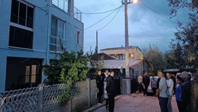 Akşam saatlerinde çekilmiş bir sokak görüntüsü var. Bir apartmanın önü ve dar bir ara sokak boyunca toplanmış insanlar görülüyor. Bazıları kapının önünde bekliyor, bazıları karşı tarafta ayakta durup konuşuyor. Sokak lambası yanıyor, ortamda merak ve tedirginlik hissi hâkim.