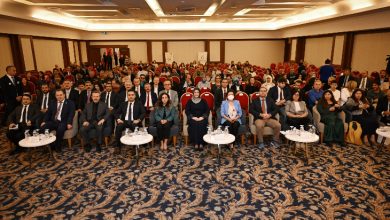 Görselde geniş bir konferans salonunda kalabalık bir katılımcı grubu görülüyor. Ön sırada resmi kıyafetli katılımcılar otururken, arkada salonu dolduran çok sayıda kişi dikkatle etkinliği takip ediyor. Ortam, bir konferans veya ödül törenine ait düzenli ve resmi bir atmosfer yansıtıyor.