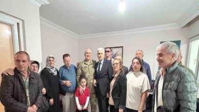 Fotoğrafta, bir araya gelmiş kalabalık bir grup görünüyor. Ortada üniformalı bir asker ile takım elbiseli bir kişi yan yana duruyor; etraflarında farklı yaşlardan kadınlar, erkekler ve bir çocuk bulunuyor. Herkes kameraya dönük, samimi ve sıcak bir aile buluşması havası var. Oda sade, duvarda bir tablo ve tavanda tek bir ampul ışığı görülüyor.