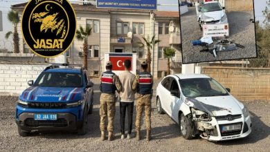 Görselde jandarma karakolunun önünde iki jandarma personeli, aralarında sivil bir kişiyi durdurmuş şekilde görülüyor. Sol tarafta mavi bir jandarma aracı, sağda ise hasarlı beyaz bir otomobil yer alıyor. Arka planda Türk bayrağı ve “Şehit Nusret Bey Jandarma Karakol Komutanlığı” tabelası dikkat çekiyor. Sol üstte JASAT logosu, sağ üstte ise araç ve delil fotoğraflarının yer aldığı küçük bir ek görsel bulunuyor.