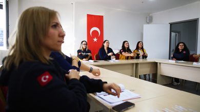 Bir eğitim salonunda, 112 Acil Sağlık personelinin masa etrafında oturarak işitme engelli bireylerle iletişim için işaret dili eğitimi aldığı, arka planda Türk bayrağının yer aldığı bir an görülüyor.