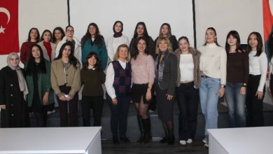 Görselde, bir üniversite salonunda yan yana dizilmiş kalabalık bir kadın grubu görülüyor. Katılımcılar kameraya doğru poz verirken arka planda projeksiyon perdesi ve Türk bayrağı yer alıyor. Sahne, akademik bir etkinlik sonrası çekilmiş toplu hatıra fotoğrafını yansıtıyor.