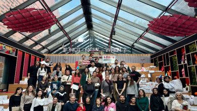 Cam tavanlı geniş bir mekânda, LÖSEV afişleri önünde toplanmış kalabalık bir grup, hediye paketleriyle birlikte kameraya poz veriyor; ortam renkli, canlı ve dayanışma hissi güçlü.