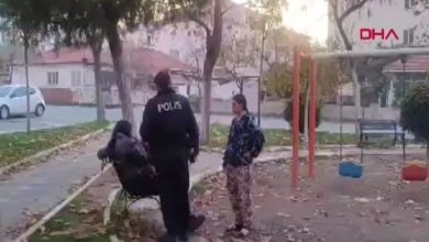 Bir parkta, üzerinde “POLİS” yazan montlu bir görevli, bankta oturan bir kişi ve yanında ayakta duran başka bir kişiyle konuşuyor; arka planda salıncaklar, ağaçlar ve apartmanlar görülüyor.