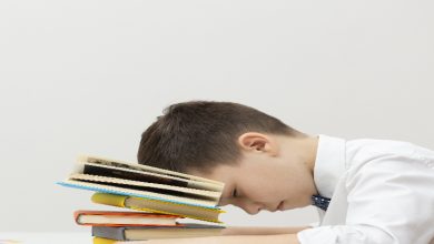 Fotoğrafta, küçük bir çocuk bir masa başında yorgun şekilde uyuklarken görülüyor. Başını, üst üste dizilmiş renkli kitapların üzerine koymuş. Üzerinde beyaz gömlek ve kravat var. Arka plan sade ve boş; bu da çocuğun yorgunluğunu ve ders yükünü daha belirgin kılıyor.