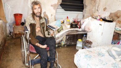 Tekerlekli sandalyede oturan Muhittin Cengiz, dökülen duvarlar, dağınık eşyalar ve yıpranmış mobilyalarla çevrili küçük ve bakımsız bir odada bulunduğu görülüyor.