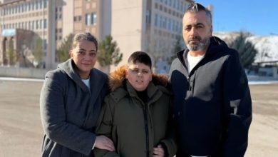 Otizmli öğrenci İsmail Doruk Sarimbeyli ortada, annesi ve babası yanında bulunuyor, arkalarında ise okul binası görünüyor.