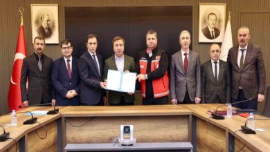 Erzincan Valisi Hamza Aydoğdu ile katılımcılar masa başında ayakta durarak, protokol belgesiyle poz veriyor.