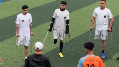 Beyaz formalı üç ampute futbolcu sahaga, karşılarında hocaları ve turuncu formalı sporcu bulunuyor.