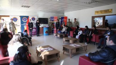 Bir salonda jandarma personelinin katılımıyla düzenlenen toplantıda, koltuklarda oturan engelli bireyler ve ailelerine yönelik bilgilendirme yapılıyor. Arka planda jandarmaya ait afişler yer alırken, ortam resmi ama sıcak bir buluşma havası taşıyor.