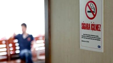 Duvara asılı “Sigara içilmez” tabelası net biçimde görünürken, arka planda balkonda oturan bir kişi bulanık şekilde siluet halinde yer alıyor. Sahne, sigara yasağını vurgulayan sakin ama mesajı net bir ortam sunuyor.