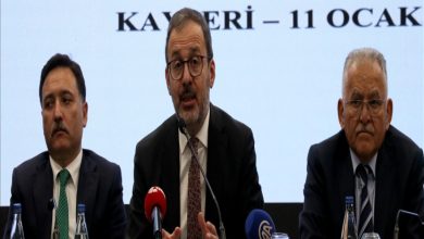 Üç erkek yetkili, mikrofonların önünde bir basın toplantısı yapıyor. Arkadaki ekranda “Kayseri – 11 Ocak” yazısı yer alıyor; ortadaki konuşmacı el hareketleriyle açıklama yaparken diğer ikisi dikkatle dinliyor. Atmosfer resmi ve ciddi.