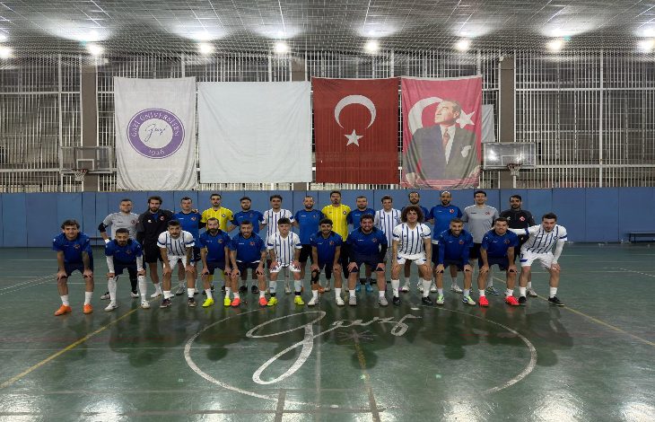 Kapalı bir spor salonunda, Türkiye İşitme Engelliler Futsal Milli Takımı toplu halde kamera karşısında dizilmiş. Mavi ve beyaz formalarla iki sıra halinde poz veriyorlar. Arkada Türk bayrağı ve Atatürk posteri asılı; salon ışıkları parlak ve düzenli.