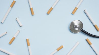 Açık mavi zemin üzerine dağınık şekilde yerleştirilmiş çok sayıda sigara görülüyor. Sağ tarafta bir stetoskop bulunuyor. Görsel, sigara kullanımının sağlık üzerindeki etkilerine ve tıbbi boyutuna dikkat çeken sembolik bir kompozisyon sunuyor.