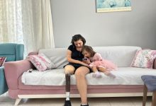 Pastel renkli bir oturma odasında, kanepede protez bacağı takılı Ece Mazı ile küçük bir kız çocuğu oturuyor. Kadının telefonuna birlikte odaklanmış halde sakin ve samimi bir an paylaşıyor.