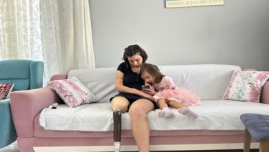 Pastel renkli bir oturma odasında, kanepede protez bacağı takılı Ece Mazı ile küçük bir kız çocuğu oturuyor. Kadının telefonuna birlikte odaklanmış halde sakin ve samimi bir an paylaşıyor.