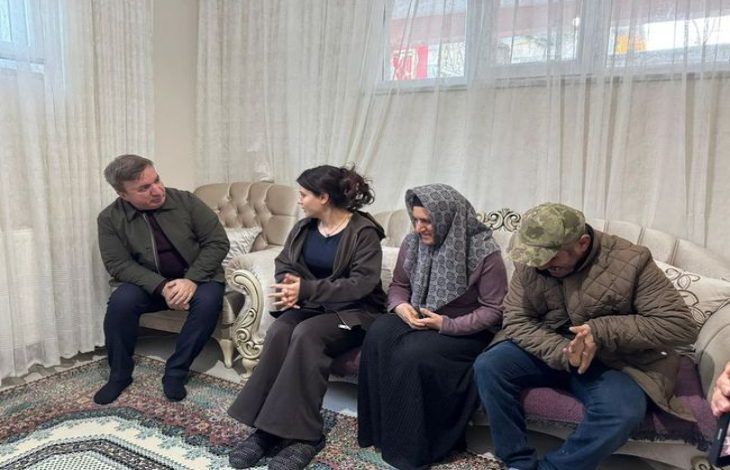 Bir ev ortamında, salonda yan yana oturan dört kişi görülüyor. Koltukta oturanlar ciddi bir sohbet içindeymiş gibi görünüyor. Ortam sade ve düzenli; arka planda tül perdeler, klasik tarzda koltuklar ve desenli bir halı dikkat çekiyor. Atmosfer samimi ve hüzünlü bir ziyaret havası taşıyor.