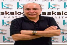 Arka planda “Kaşkaloğlu Göz Hastanesi” logosunun tekrar ettiği bir fon önünde, siyah polo tişört giymiş bir erkek kollarını göğsünde bağlamış şekilde poz veriyor. Gülümsüyor ve kameraya doğrudan bakıyor; bileğinde metal kayışlı bir saat bulunuyor. Görsel, kurumsal bir çekim izlenimi veriyor.