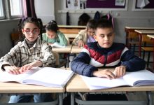 Sıralarda oturan görme engelli erkek ve kız öğrenciler braille yazılı kitapçığa dokunuyor.