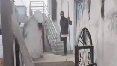 Dar ve taş bir geçitte, merdivenlerin bulunduğu eski bir yapı görülüyor. Merdiven başında elinde sopa benzeri bir nesne tutan bir kişi ayakta duruyor; çevrede duvarlar, metal korkuluklar ve giriş kapıları yer alıyor.