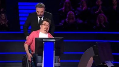 Bir televizyon yarışma programı stüdyosunda, tekerlekli sandalyede oturan bir yarışmacı ekran karşısında bulunuyor. Arkasında sunucu ayakta duruyor. Sahne mavi ışıklarla aydınlatılmış; arka planda seyirci sıraları seçiliyor. Yarışmacı duygusal bir an yaşıyor gibi görünürken, sunucu destekleyici bir duruş sergiliyor.