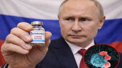 Takım elbiseli bir erkek, arka planda Rusya bayrağı önünde küçük bir flakonu kameraya doğru tutuyor. Flakonun üzerinde “ENTEROMIX – Cancer Vaccine” yazıyor. Görselin sağ alt köşesinde ise kanser hücrelerini temsil eden illüstratif bir mikroskobik görsel yer alıyor.