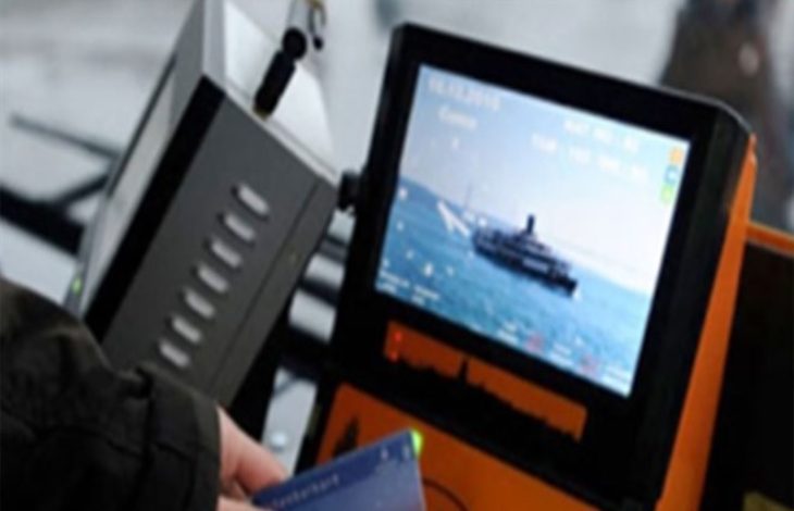 Bir toplu taşıma aracında yer alan elektronik kart okuma cihazı görülüyor. Ekranda deniz üzerinde ilerleyen bir vapur görüntüsü yer alıyor. Ön planda bir kişi ulaşım kartını cihaza tutuyor. Görsel, toplu taşımada kartlı geçiş sistemini ve elektronik bilet uygulamasını yansıtıyor.