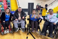 Görselde, kapalı bir spor salonunda tekerlekli sandalyeleri üzerinde yan yana dizilmiş dört sporcu bir arada görülmektedir.