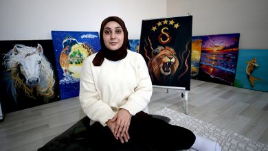 Fotoğrafta bir odada yerde oturan genç bir kadın görülüyor. Başörtülü olan kadın açık renk bir kazak giymiş ve kameraya doğru sakin bir ifadeyle bakıyor. Arka planda duvara dayalı şekilde sergilenen birkaç tablo bulunuyor. Tablolarda beyaz bir at, aslan figürü ve gün batımı manzarası gibi farklı resimler yer alıyor. Kadın, kendi yaptığı resimlerin önünde oturarak poz veriyor.