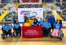 Bir spor salonunda, tekerlekli sandalyeli sporculardan oluşan Gaziantep Boccia Takımı, "Türkiye Boccia Şampiyonası" panosu önünde toplu poz veriyor. Sporcuların önünde "Büyükşehir Gaziantep" yazılı kırmızı bir bayrak açılmış durumda. Arka planda tribünler ve Türk bayrağı görülüyor.