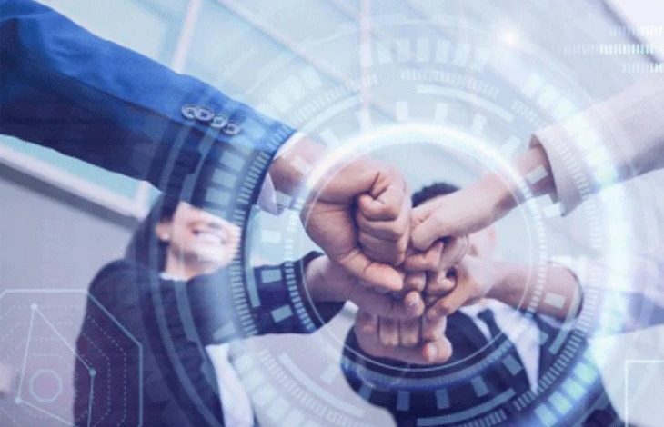 Mavi tonların hakim olduğu görselde, merkezde üst üste kenetlenmiş eller etrafında dijital halkalar ve teknoloji grafikleri yer alıyor. Arka planda ise iş birliğini simgeleyen, gülümseyen takım elbiseli profesyoneller görülüyor; genel tema birlik ve inovasyon.