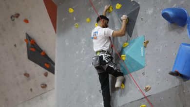 Görselde, bir sporcu yapay tırmanış duvarında yukarı doğru ilerliyor. Duvar üzerinde farklı renklerde tutamaklar bulunuyor ve sporcu emniyet ipine bağlı durumda. Odak, tırmanış sırasında sporcuların güç ve denge gerektiren hareketlerine verilmiş. Arka planda Fethiye’de düzenlenen bir para tırmanış antrenmanının atmosferi yansıyor.