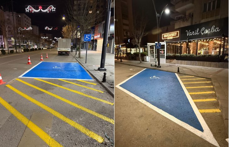 Görselde, gece saatlerinde bir şehir caddesinde engelli bireyler için ayrılmış park alanları görülüyor. Mavi zemin üzerine tekerlekli sandalye sembolü çizilmiş ve sarı çizgilerle park sınırları belirlenmiş. Yol kenarında yer alan bu alanlar, engelli sürücülerin araçlarını rahatça park edebilmesi için düzenlenmiş özel park yerlerini gösteriyor. Arkada mağazalar ve sokak aydınlatmaları da dikkat çekiyor.