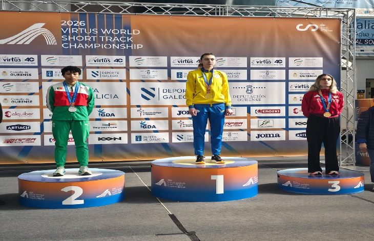 Fotoğrafta bir spor müsabakasının ödül töreni görülüyor. Üç sporcu madalya kürsüsünde yer alıyor. Ortada birinci olan sporcu en yüksek basamakta altın madalyayla dururken, solda ikinci olan sporcu gümüş madalya ile ikinci basamakta bulunuyor. Sağda ise üçüncü basamakta bronz madalya kazanan bir sporcu yer alıyor. Arka planda “2026 Virtus World Short Track Championship” yazılı sponsor panosu bulunuyor ve sporcular boyunlarında madalyalarıyla kürsüde poz veriyor.