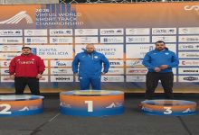 Görselde uluslararası bir atletizm şampiyonasının ödül töreni görülüyor. Üç sporcu podyumda yer alırken, ikinci sıradaki sporcu Türkiye eşofmanıyla kürsüde duruyor. Arkada yarışmanın sponsor ve organizasyon panosu bulunuyor.