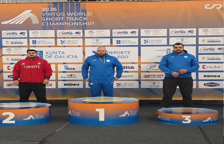 Görselde uluslararası bir atletizm şampiyonasının ödül töreni görülüyor. Üç sporcu podyumda yer alırken, ikinci sıradaki sporcu Türkiye eşofmanıyla kürsüde duruyor. Arkada yarışmanın sponsor ve organizasyon panosu bulunuyor.