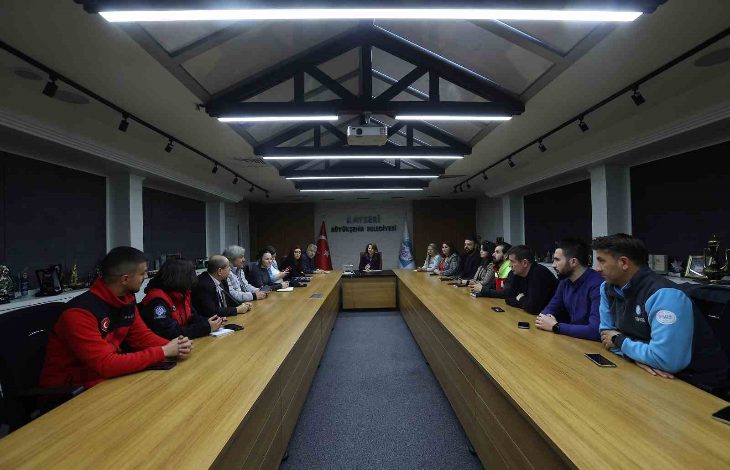 Uzun bir toplantı masasının etrafında toplanmış katılımcılar, resmi bir toplantı yapıyor. Masanın başında bir yetkili otururken, iki yanda farklı kurumlardan gelen kişiler dikkatle dinliyor. Ortam, belediyeye ait bir toplantı salonunu andırıyor ve ciddi bir çalışma atmosferi hâkim.