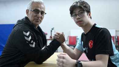 Fotoğrafta bir masa başında karşılıklı oturan iki kişi görülüyor. Biri orta yaşlı, diğeri genç olan iki kişi ellerini kenetleyerek bilek güreşi pozisyonu almış. Genç olan kişi Türkiye bayrağı bulunan spor tişörtü ve gözlük takıyor. İkisi de kameraya bakarken spor ve antrenman ortamını andıran bir mekânda bulunuyor.