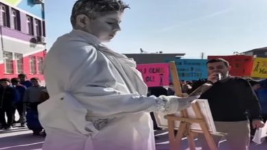 Okul bahçesinde düzenlenen farkındalık etkinliğinde, tamamen beyaza boyanmış bir öğrenci heykel performansı sergiliyor ve tuval üzerine resim yapıyor. Etrafında toplanan öğrenciler etkinliği izlerken, arka planda mesaj içeren pankartlar dikkat çekiyor. Atmosfer, bağımlılık ve farkındalık temalı bir sosyal sorumluluk çalışmasını yansıtıyor.