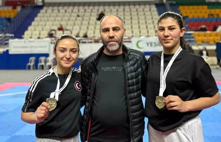 Bir spor salonunda çekilmiş fotoğrafta, ortada bir erkek ve iki yanında spor kıyafetli iki kadın yer alıyor. Kadın sporcular boyunlarında madalya taşıyor ve kameraya gülümseyerek poz veriyor. Arka planda tribünler ve minderli bir müsabaka alanı görülüyor.