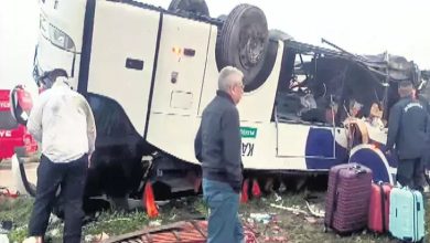 Görselde, devrilmiş bir yolcu otobüsü ve çevresinde inceleme yapan kişiler görülüyor. Otobüs yan yatmış durumda; bagajlar, kişisel eşyalar ve kırılmış parçalar etrafa dağılmış. Olay yeri görevlileri ile bazı siviller kazanın olduğu alanda inceleme yapıyor. Genel atmosfer acil durum müdahalesinin sürdüğünü gösteriyor.