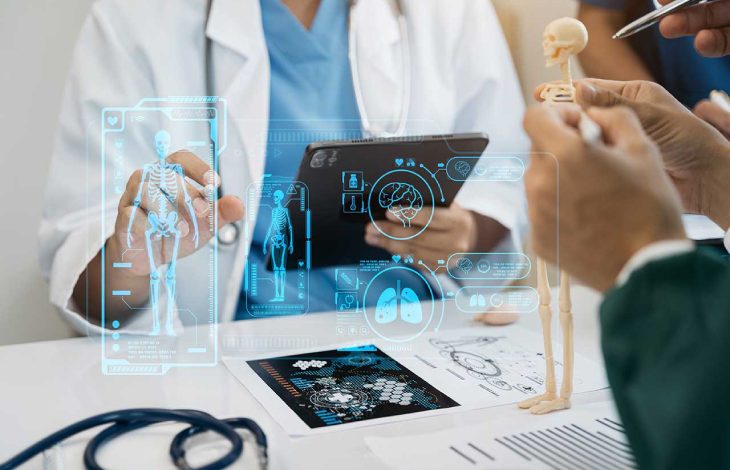 Bu görselde, bir sağlık çalışanı tablet kullanarak dijital bir sistem üzerinden insan iskeleti ve organlarını incelemekte, aynı zamanda masanın üzerinde küçük bir iskelet modeli ile insan anatomisi hakkında açıklama yapılmaktadır.