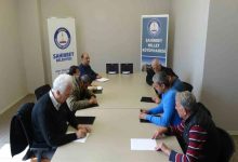 Bir toplantı salonunda çekilen fotoğrafta, uzun bir masa etrafında oturan birkaç yetişkin kişi Braille alfabesi (kabartma yazı) öğrenmek için önlerindeki kâğıt ve kabartma yazı tabletleri üzerinde çalışıyor. Arka tarafta Şahinbey Belediyesi ve Şahinbey Millet Kütüphanesi yazılı afişler yer alıyor. Katılımcılar sessiz bir ortamda not alarak eğitime odaklanmış görünüyor.