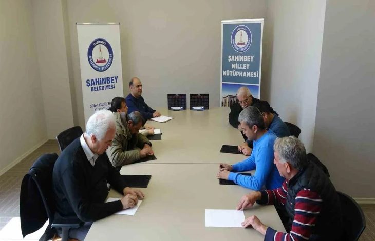 Bir toplantı salonunda çekilen fotoğrafta, uzun bir masa etrafında oturan birkaç yetişkin kişi Braille alfabesi (kabartma yazı) öğrenmek için önlerindeki kâğıt ve kabartma yazı tabletleri üzerinde çalışıyor. Arka tarafta Şahinbey Belediyesi ve Şahinbey Millet Kütüphanesi yazılı afişler yer alıyor. Katılımcılar sessiz bir ortamda not alarak eğitime odaklanmış görünüyor.