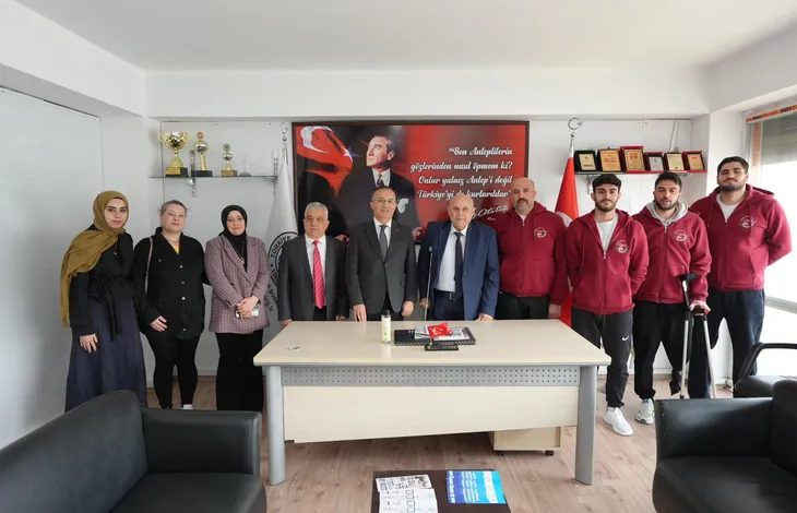 Fotoğrafta bir dernek ofisinde çekilmiş toplu bir kare görülüyor. Masanın arkasında takım elbiseli yöneticiler ve yanlarında farklı yaşlardan kadın ve erkeklerden oluşan bir grup yan yana duruyor. Sağ tarafta bordo eşofmanlı birkaç genç de gruba eşlik ediyor; içlerinden biri koltuk değneği kullanıyor. Arka duvarda büyük bir Mustafa Kemal Atatürk portresi ve Türk bayrağı bulunan kırmızı bir pano yer alıyor. Sol tarafta raf üzerinde kupalar ve ödüller görülürken, odada bir masa, sandalyeler ve koltuklar bulunuyor. Grup kameraya dönük şekilde poz veriyor.