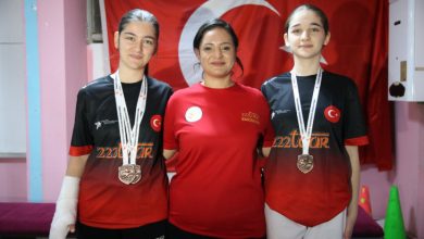 İşitme engelli tekvandocu Beren Su ile Selen Naz Ulus'un ortasında tekvando antrenörü Büşra Benzer bulunuyor ve Türk bayrağı önünde poz veriyorlar.