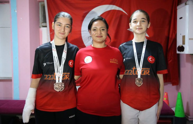 İşitme engelli tekvandocu Beren Su ile Selen Naz Ulus'un ortasında tekvando antrenörü Büşra Benzer bulunuyor ve Türk bayrağı önünde poz veriyorlar.