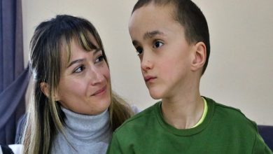 Bir odada çekilmiş fotoğrafta, kısa saçlı küçük bir çocuk yana doğru bakarken, yanında oturan bir kadın ona sevgi ve dikkatle bakıyor. Kadının yüzünde hafif bir tebessüm var; aralarındaki bağ sıcak ve koruyucu bir his veriyor. Çocuk ise düşünceli ve biraz dalgın görünüyor.